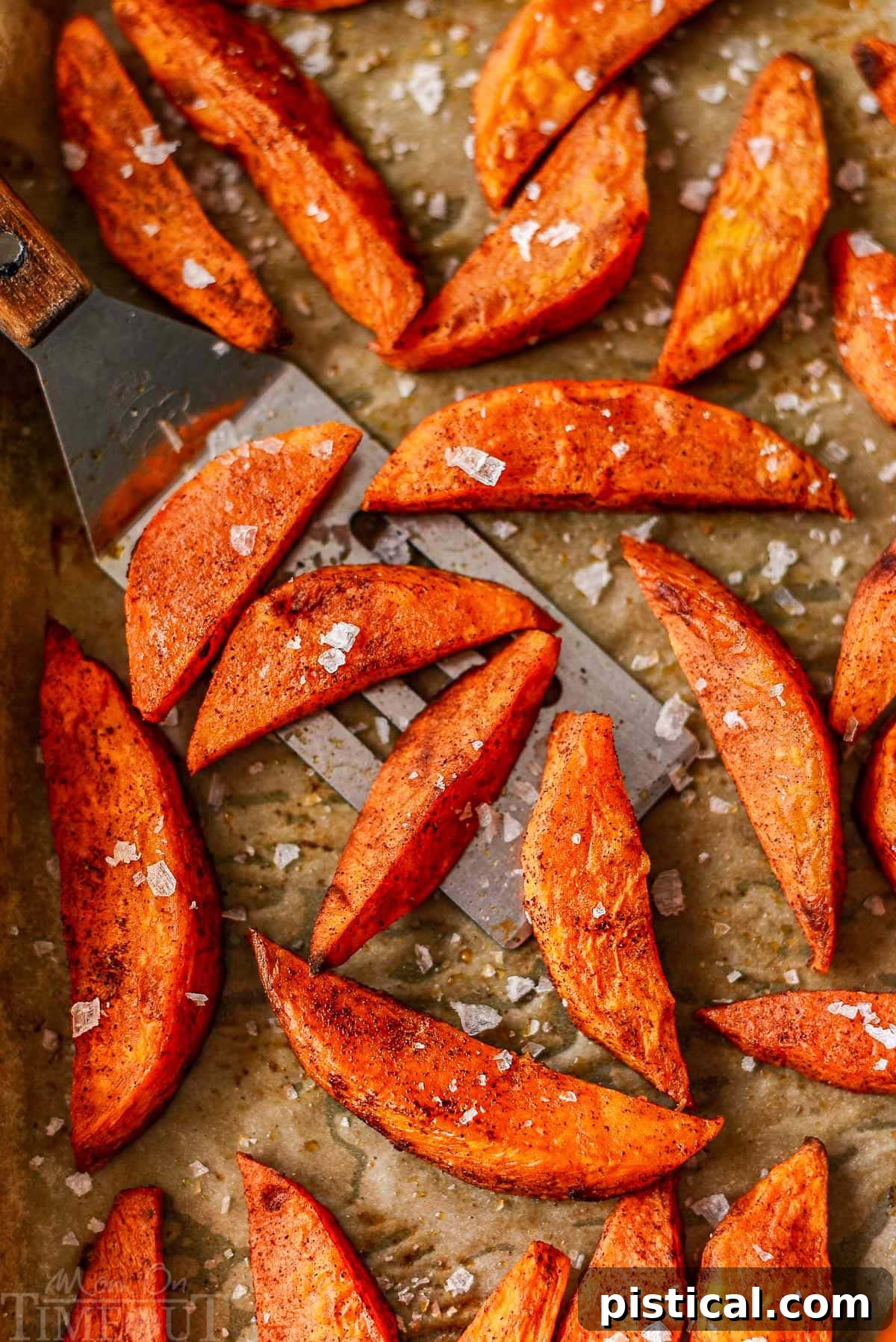 Top-down view of perfectly roasted sweet potato wedges cooling on a parchment-lined baking sheet, showcasing their golden-brown finish.