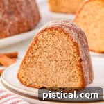Piece of apple cider donut cake on round white plate. More pieces can be seen in the background.