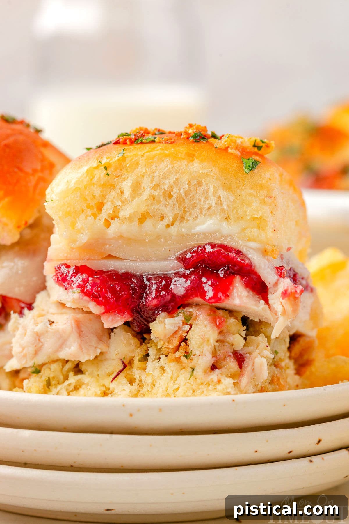 A single, perfectly assembled turkey slider resting on small, stacked white plates, showcasing the layers of filling and soft Hawaiian roll.
