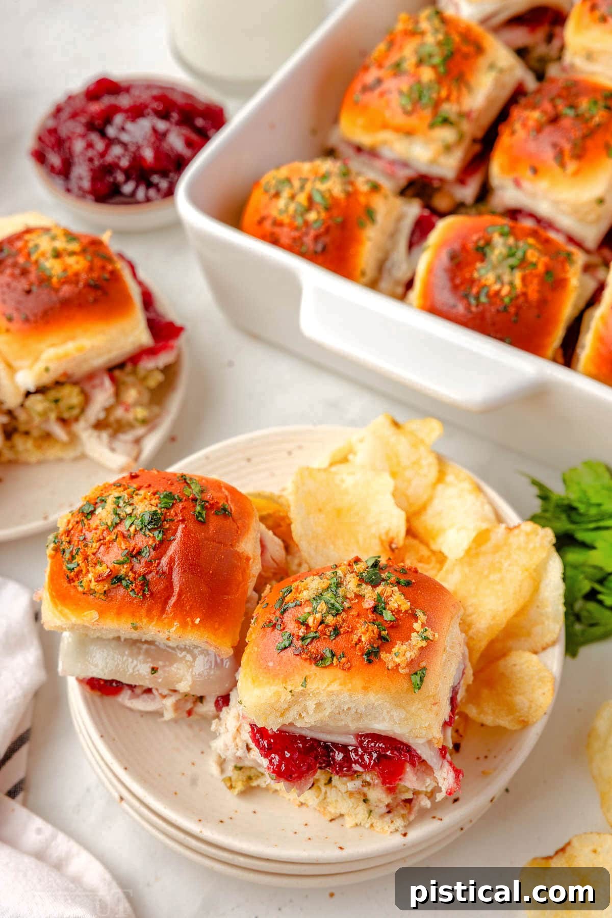 Two turkey sliders on a white plate with potato chips, and the full baking dish in the background, ready for serving.