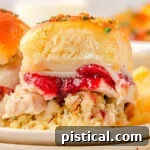 Two Turkey sliders sitting on small round plates stacked three high. Cranberry sauce, juicy turkey, and stuffing can all be seen in between the soft hawaiian roll.
