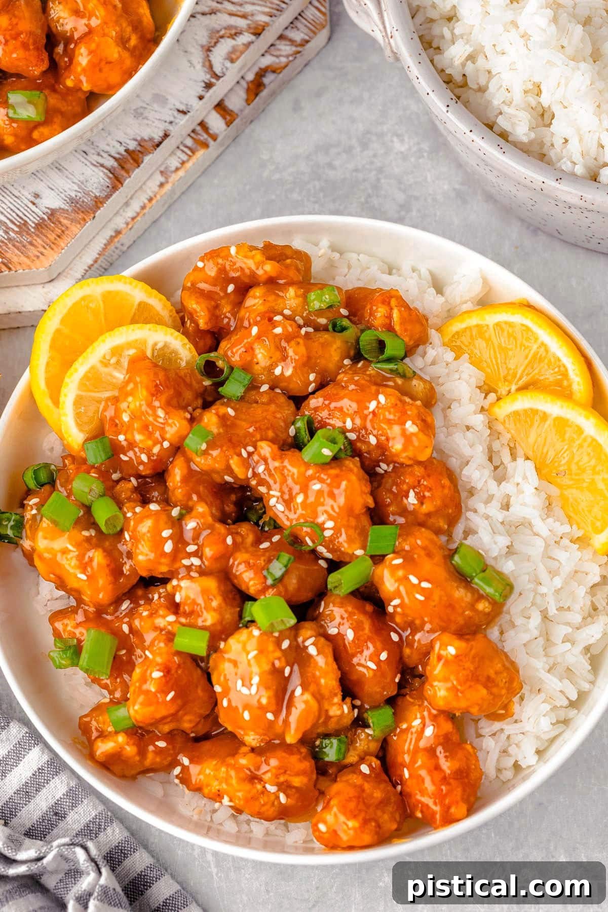 Overhead shot of lemon chicken and white rice on round plate with lime slices and green onions for garnish. Delicious Chinese Lemon Chicken is served with rice and garnished with fresh lemon and green onions.