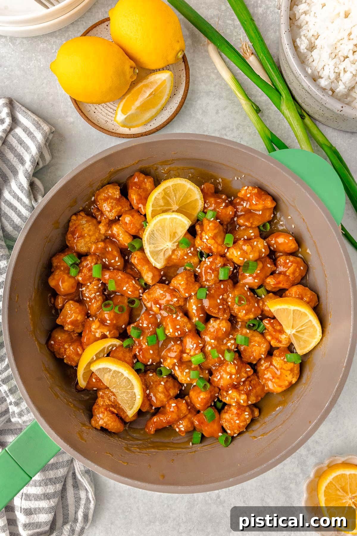 Overhead shot of skillet of chinese lemon chicken ready to be served. Garnished with slices of lemon and green onions. A skillet full of crispy Chinese Lemon Chicken, garnished with fresh lemon slices and vibrant green onions.