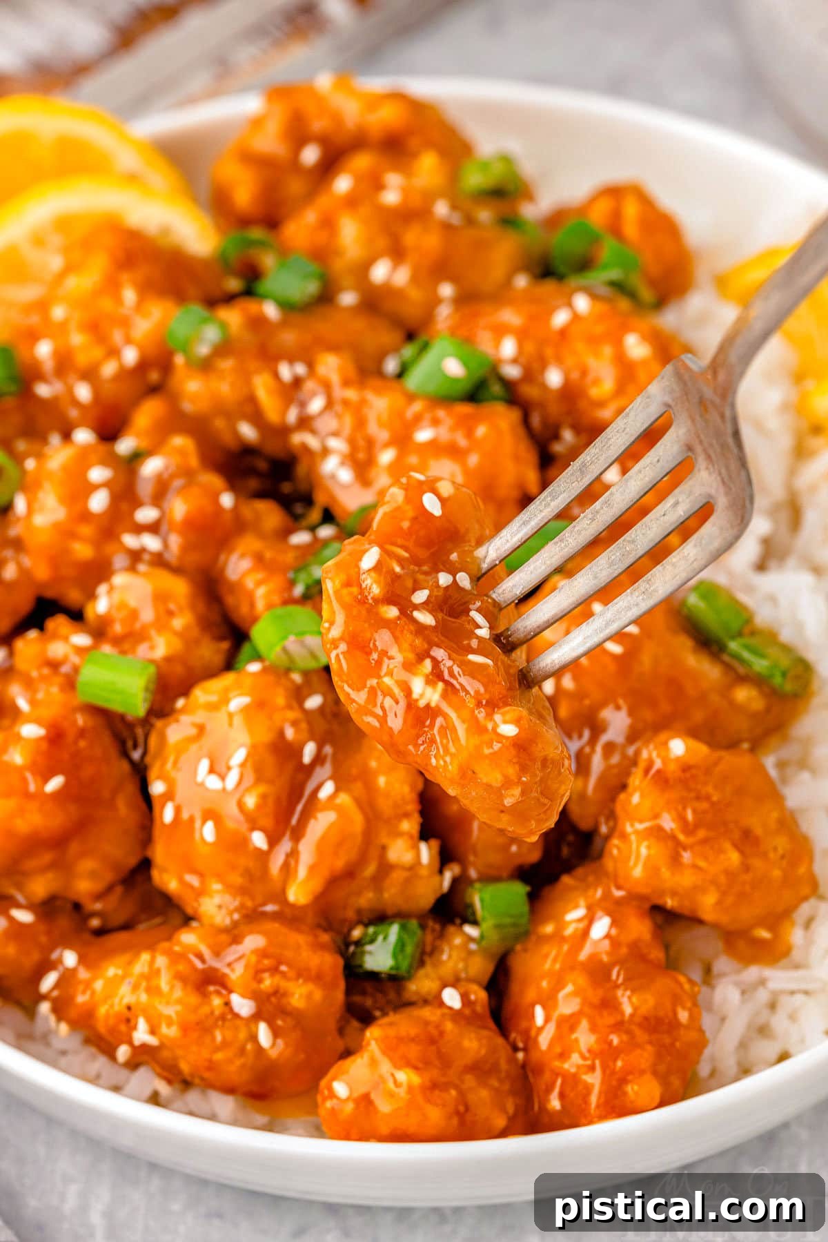Bite of lemon chicken chinese on fork being lifted away from plate of chinese lemon chicken. A fork lifting a delicious bite of Chinese Lemon Chicken, showing its crispy coating and glistening sauce.