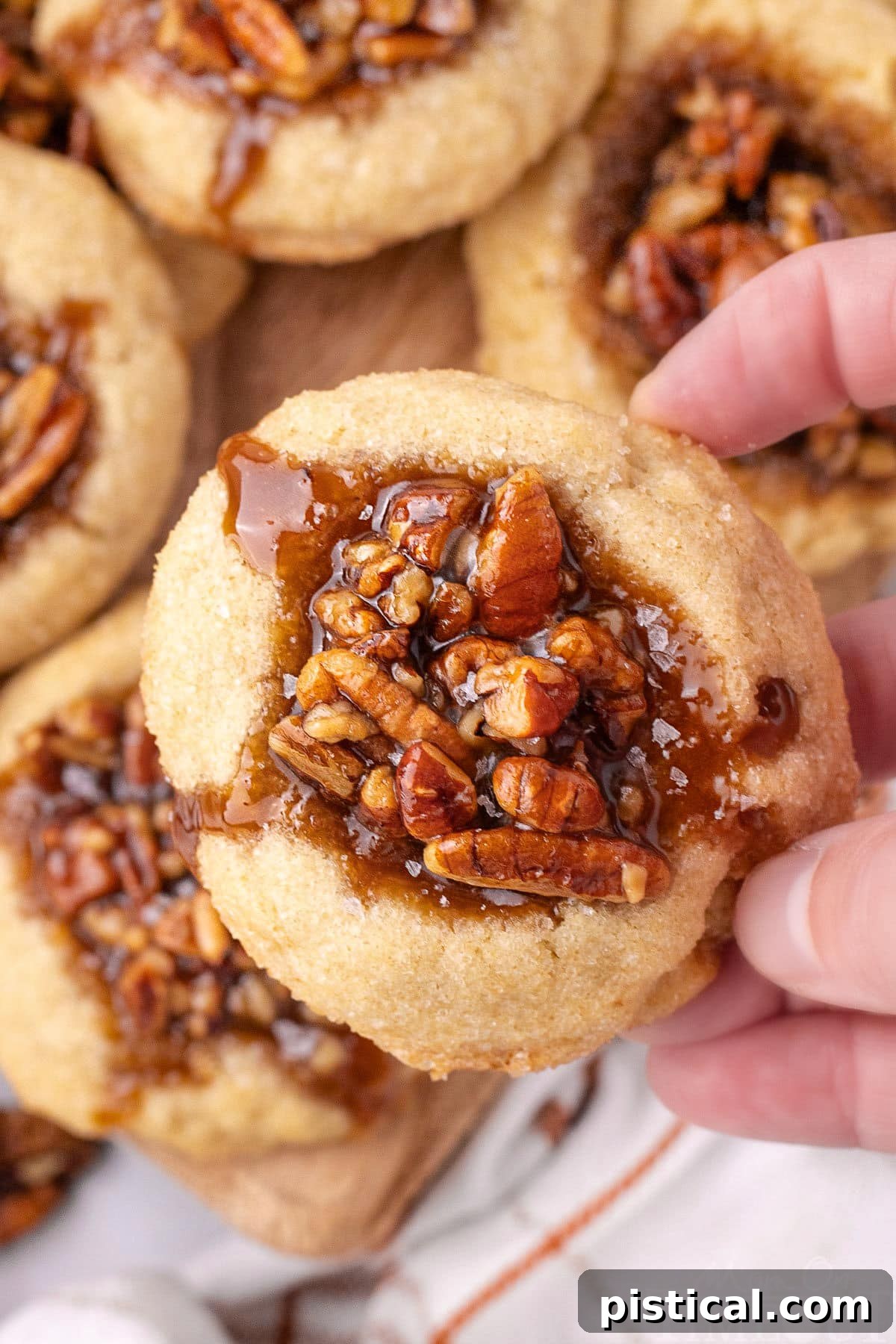 Pecan pie thumbprint cookies lifted off the board with a hand, showcasing their gooey center.