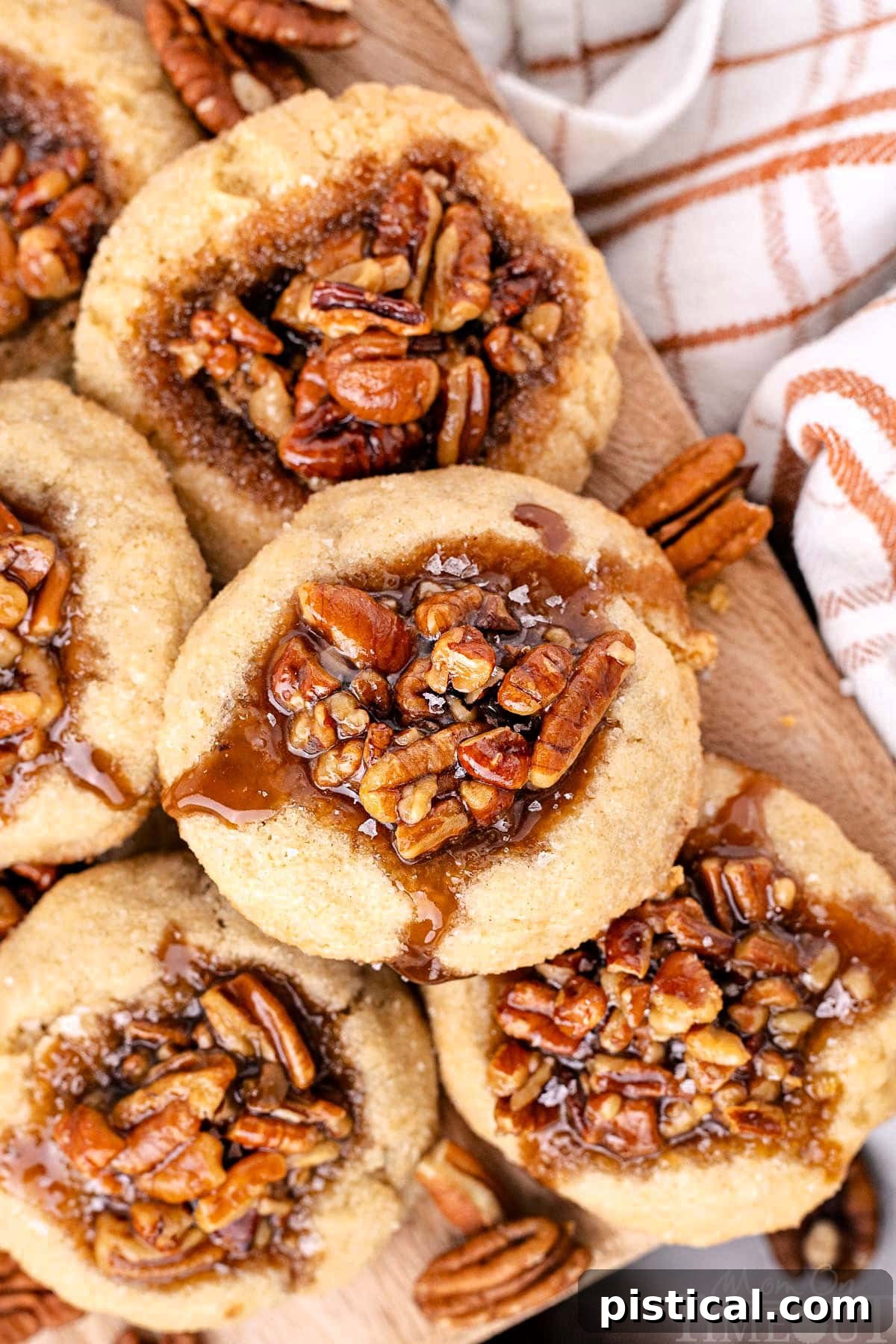 Overhead shot of pecan pie cookies piled high on a wood board next to a checked linen.