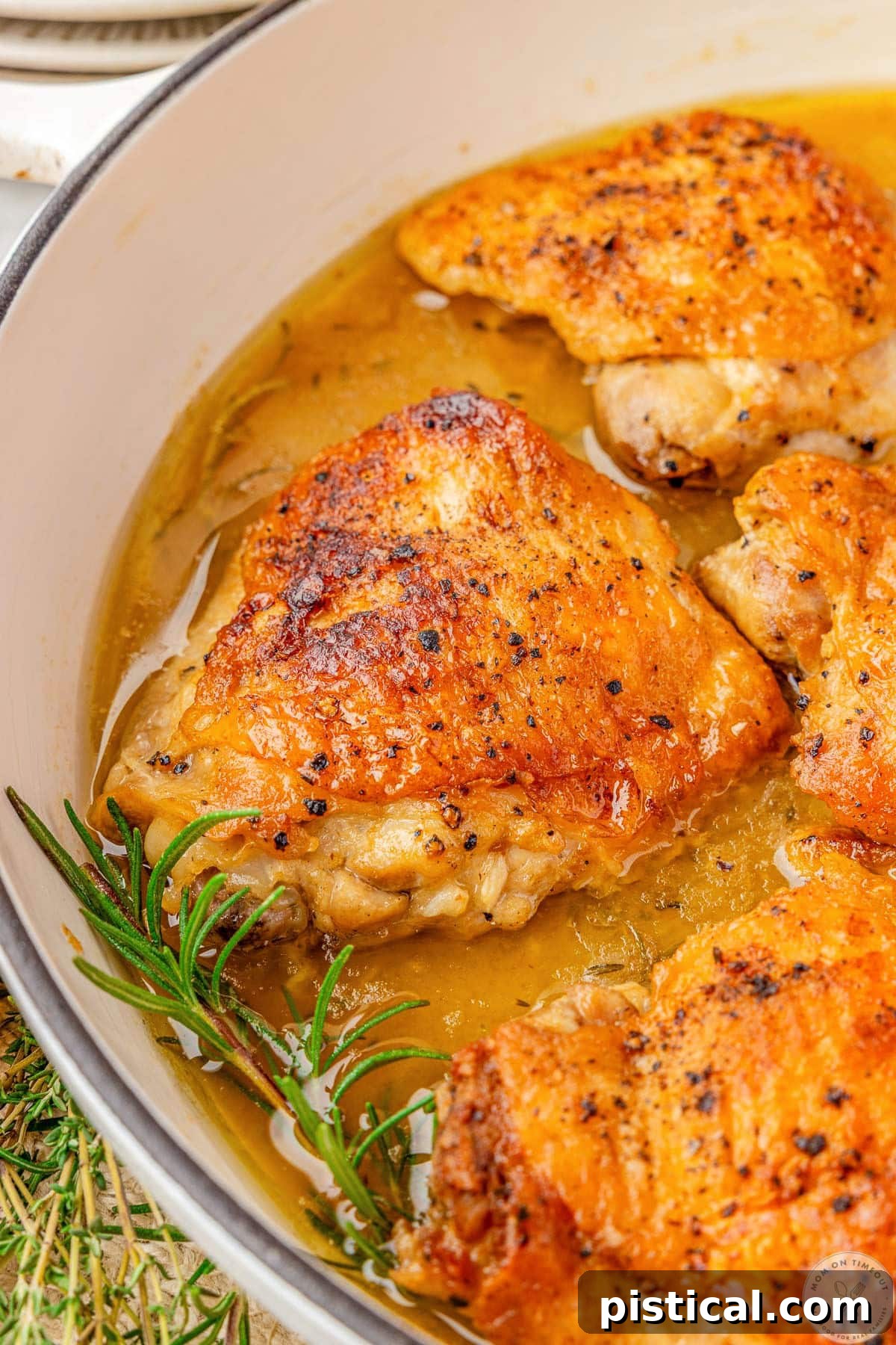 Close up look at braised chicken thighs in braiser with lemon herb sauce and fresh herbs.