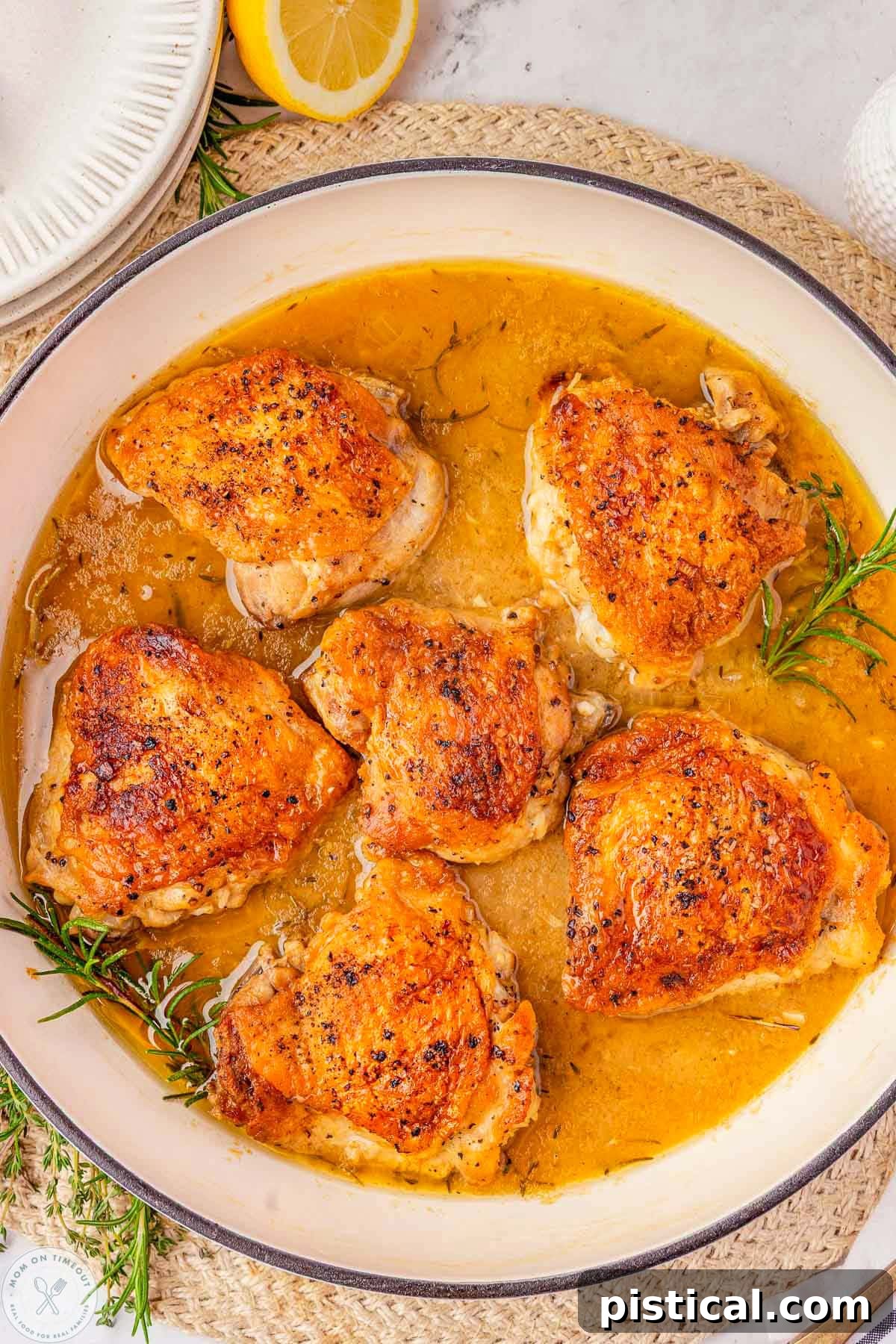 Close up overhead shot of braised chicken thighs in skillet with fresh herbs and lemon.
