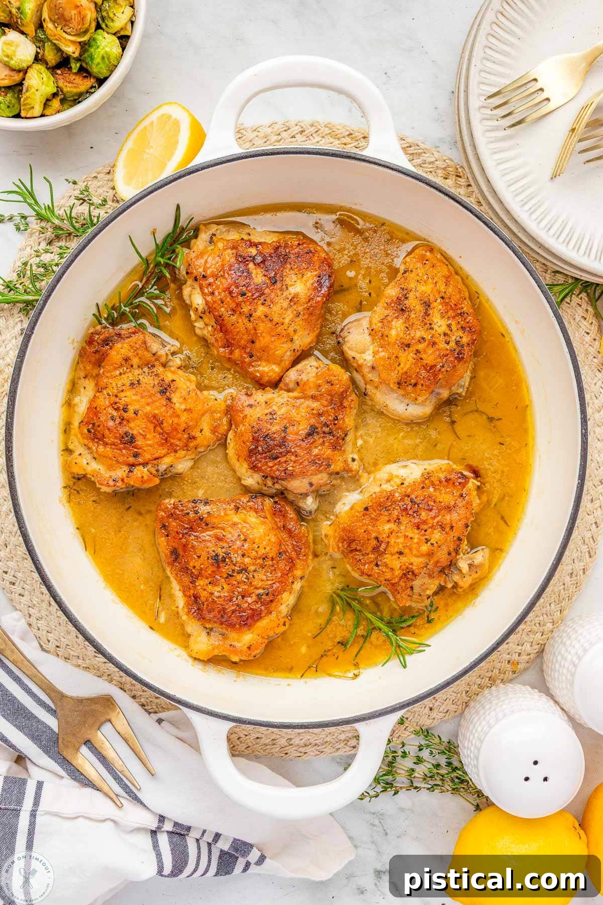 Overhead shot of large white skillet with braised chicken thighs and rosemary and thyme sprigs in the pan.