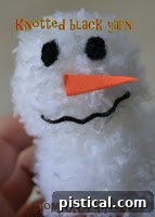 Attaching a small orange foam carrot nose to the pom pom snowman's head