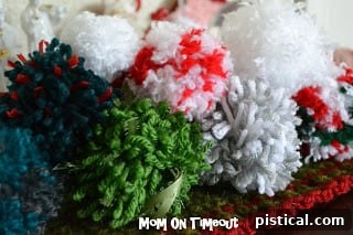 Colorful yarn balls and finished pom poms on a rustic wooden surface, highlighting the joy of yarn crafts.