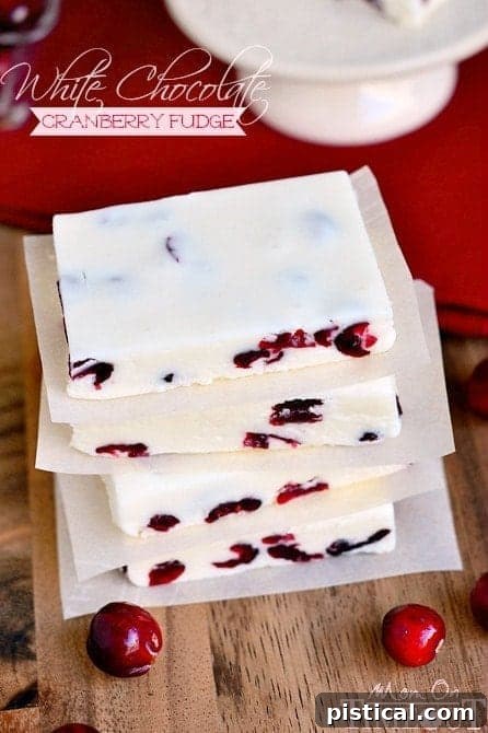 Various squares of white chocolate cranberry fudge arranged on a rustic wooden board, ready for serving.
