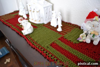 The finished red and green crocheted Christmas runner elegantly displayed on a fireplace mantel, adding a festive touch to holiday decor.