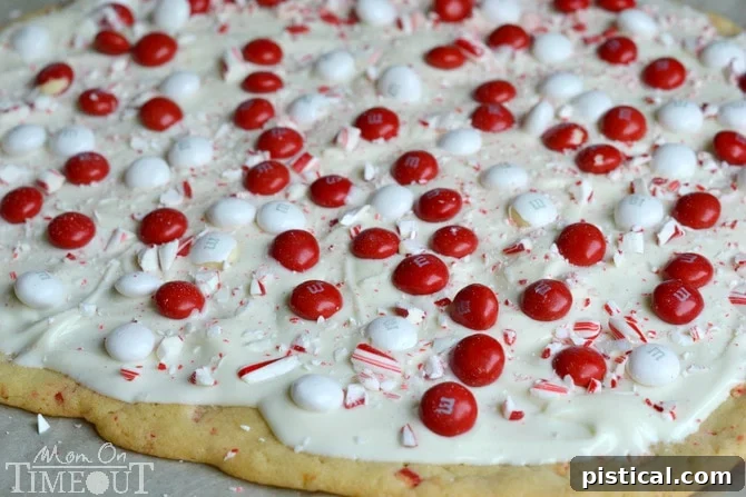 White chocolate layer with peppermint M&Ms and crushed candy canes on baked sugar cookie