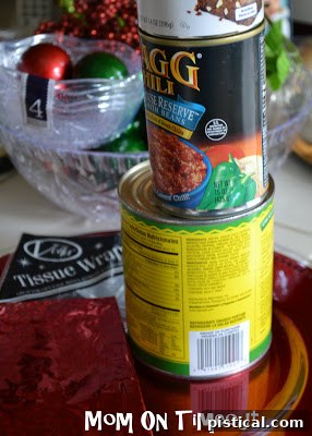 Empty cans wrapped with festive red and gold wrapping paper, ready to be used as stands for a DIY Christmas centerpiece