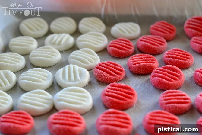 Hands carefully rolling a festive green peppermint patty dough ball in a bowl of granulated sugar, creating a sparkly coating.