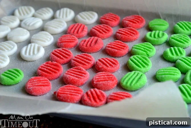 A fork gently pressing down on a vibrant red peppermint patty dough ball to flatten it and create a decorative pattern.