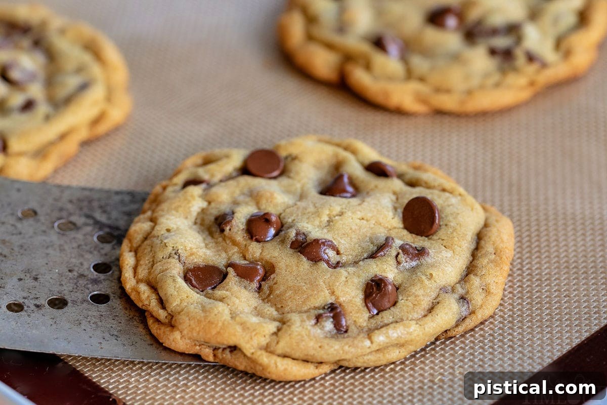 chocolate chip cookie being removed from silicone baking mat with metal spatula