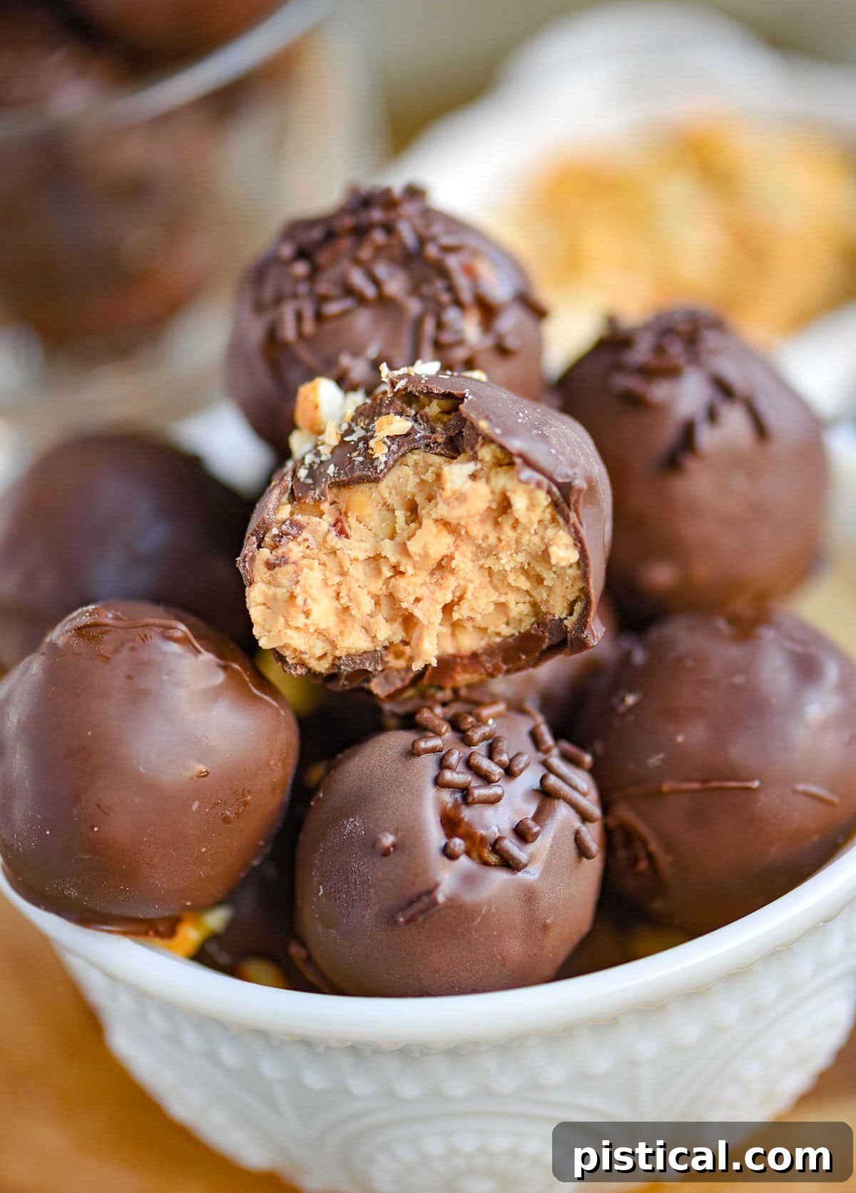 Peanut Butter Chocolate Crunch Bites 2 A white glass bowl overflowing with beautifully crafted peanut butter balls with rice krispies, each adorned with a sprinkle of chocolate jimmies or finely crushed peanuts, ready for enjoyment.