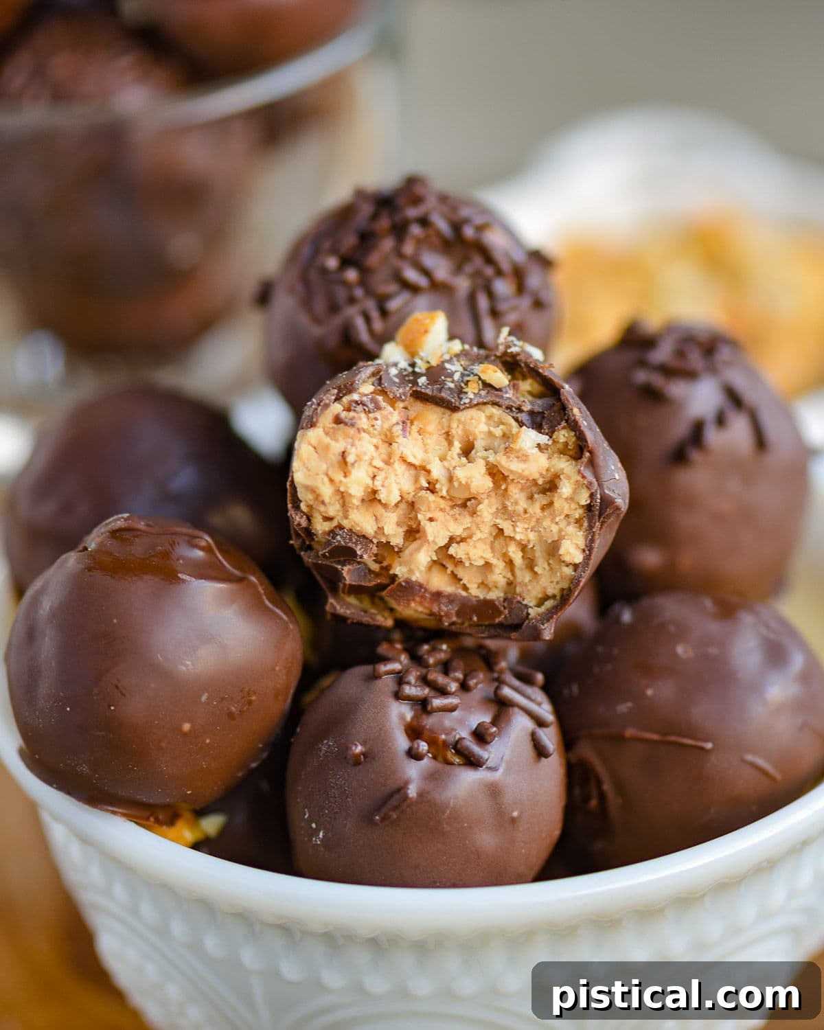 Peanut Butter Chocolate Crunch Bites 6 A white glass bowl elegantly holds a generous assortment of chocolate peanut butter balls with rice krispies, each topped with either delicate chocolate jimmies or crunchy crushed peanuts, showcasing their enticing appeal.