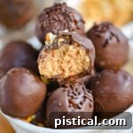 A white glass bowl filled with peanut butter balls with rice krispies. each ball is topped with either chocolate jimmies or crushed peanuts.