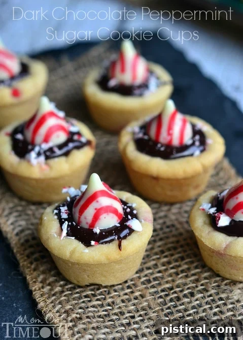Dark Chocolate Peppermint Sugar Cookie Cups filled with chocolate ganache and topped with Candy Cane Hershey's Kisses. | MomOnTimeout.com #christmas #recipe A collection of Dark Chocolate Peppermint Sugar Cookie Cups, beautifully garnished with Hershey's Kisses and crushed candy canes, ready for holiday serving.