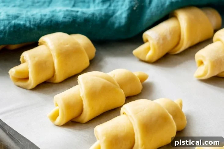 Pillowy Soft Homemade Crescent Rolls 6 Crescent rolls rising on a baking sheet, preparing for baking