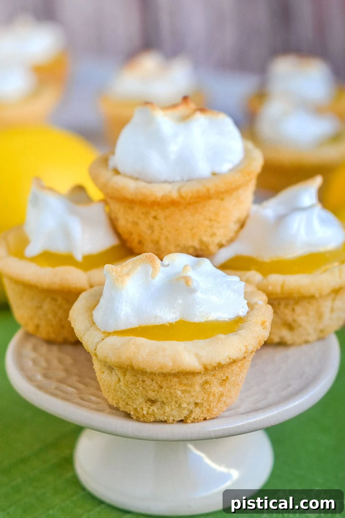 A close-up shot of Lemon Meringue Cookie Cups, neatly arranged. The crispy sugar cookie base is visible, holding a generous dollop of golden lemon curd, crowned with a peak of perfectly toasted meringue. The colors are vibrant and appetizing.