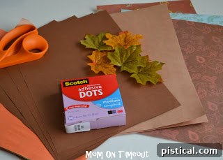 Materials for making a DIY Thanksgiving gratitude tree: fall-colored paper, leaf template, scissors, and adhesive.