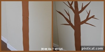 Attaching brown paper tree trunk and branches to a wall using adhesive for a DIY Thanksgiving craft.