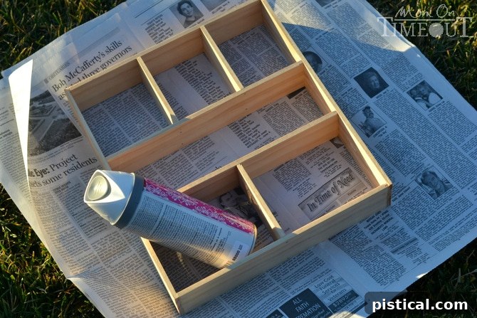 Wooden drawer dividers being spray painted white on a protective surface outdoors.