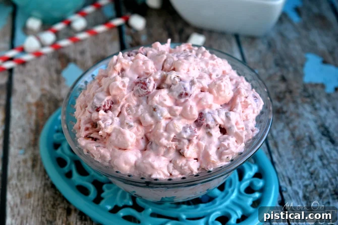 Close-up shot of creamy pink Cherry Fluff dessert salad in a clear glass bowl, resting on a blue decorative trivet, highlighting its fluffy texture.