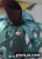 Applying glue to the base of a paper tendril before attaching it to the inside of the pumpkin for a natural, flowing look.