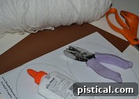An array of simple craft materials laid out on a counter, including a glue stick, a hole punch, scissors, a stack of brown paper, and a spool of white yarn, ready for the paper football craft project.