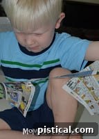 A young boy with focused expression, tearing pieces of newspaper into shreds with his hands, preparing stuffing for the paper football craft.