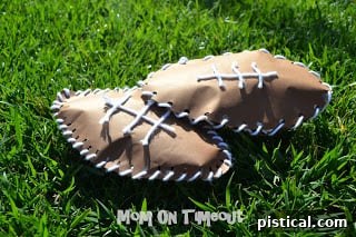 A trio of homemade paper footballs, made from brown construction paper and white yarn, resting casually on green grass, ready for an impromptu game or display.