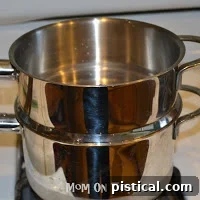 Double boiler setup on a stovetop with water simmering in the bottom pan.