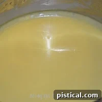 Hollandaise sauce thickening in a double boiler, showing a creamy, light yellow color.