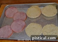 Canadian bacon slices and English muffin halves on a baking sheet, ready for the oven.