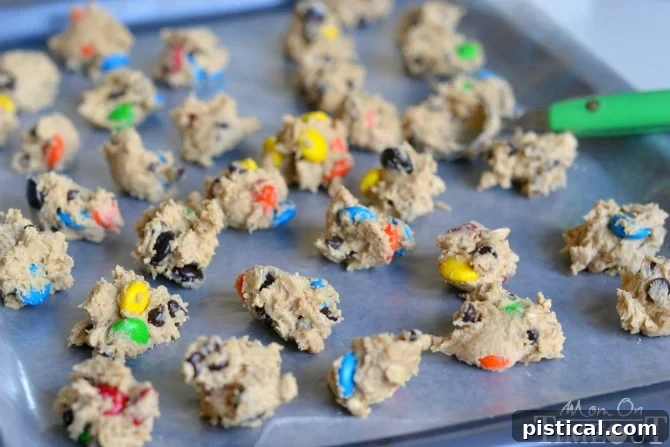Eggless edible Monster Cookie Dough being scooped into small, bite-sized balls on a baking sheet lined with waxed paper, preparing them for flash freezing.