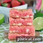 Strawberry Lime White Chocolate Dream Bars 2 stacked strawberry gooey bars four high on green and white napkin with cut limes and fresh strawberries in background.