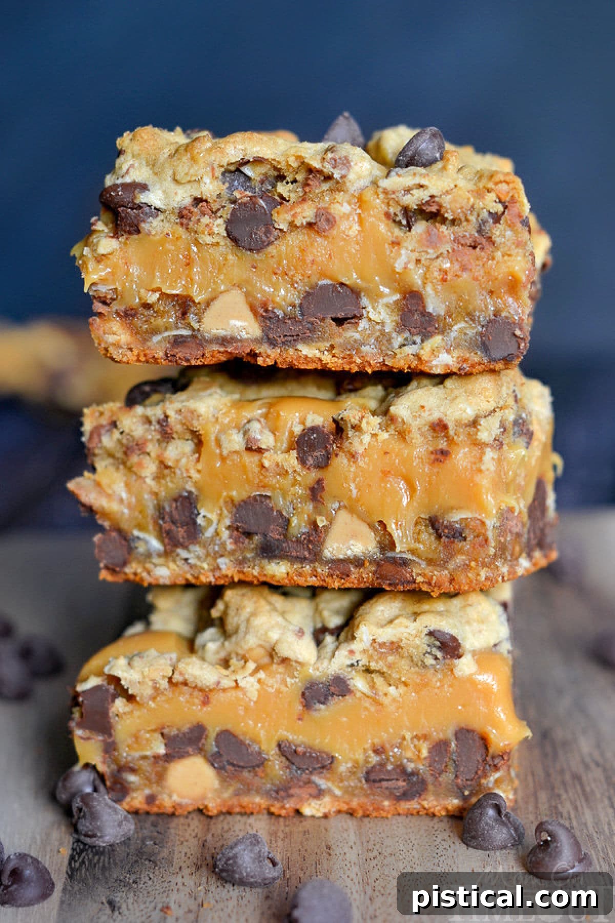 A close-up view of stacked peanut butter caramel toffee chocolate chip cookie bars on a wood cutting board, showcasing their rich textures and layers.