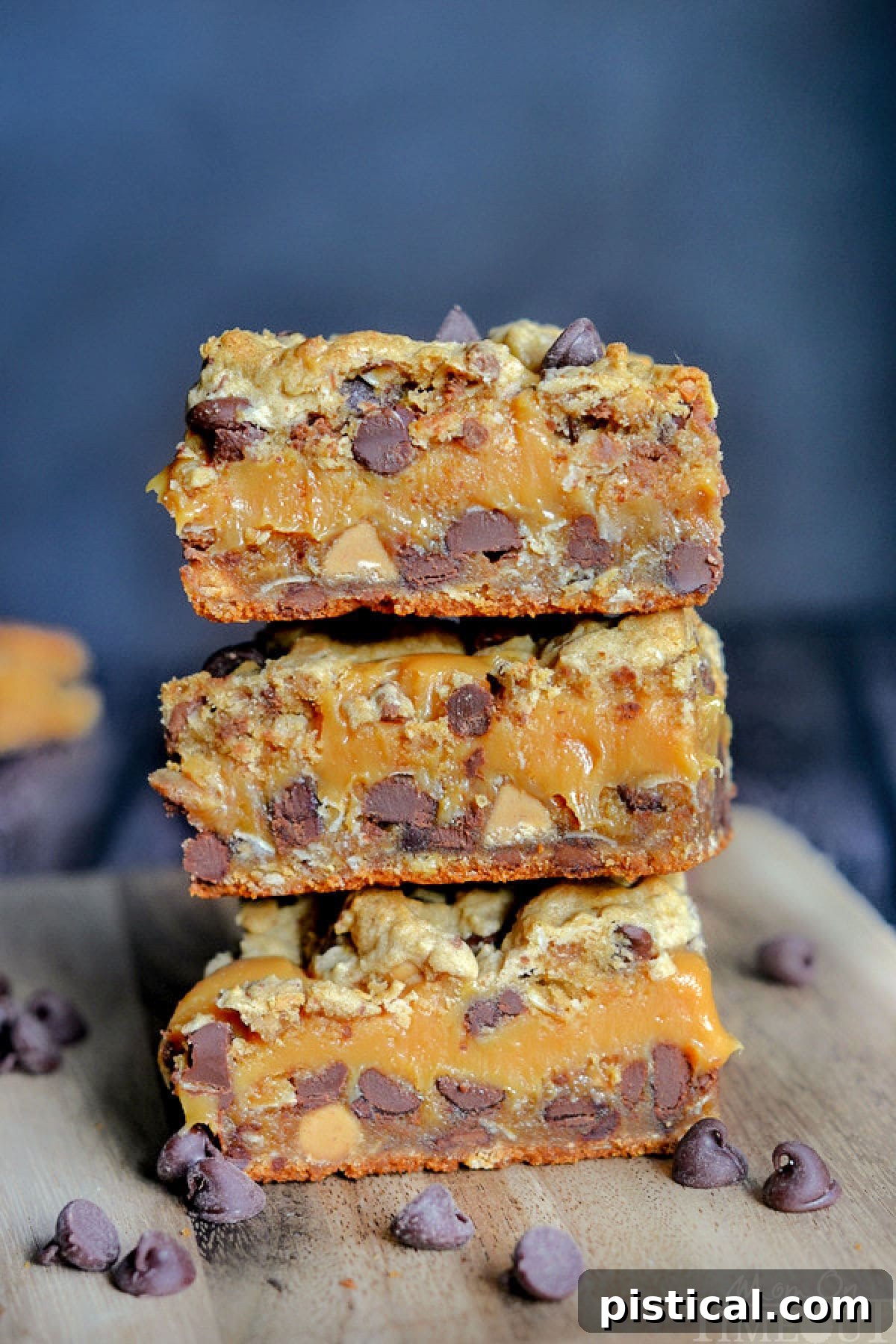 Stacked peanut butter caramel toffee chocolate chip cookie bars on a rustic wooden cutting board, highlighting the rich texture and delicious layers.