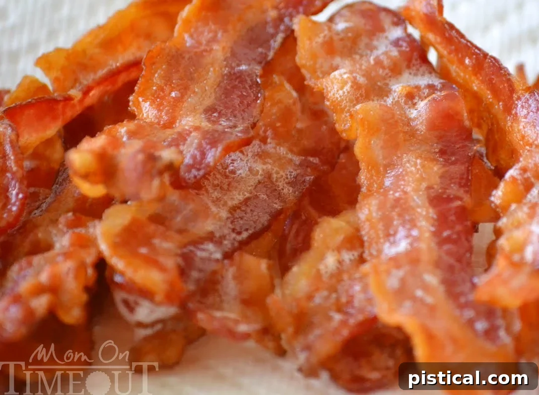 Crispy bacon strips cooking evenly on a baking sheet in the oven, demonstrating the mess-free and perfectly straight results of oven baking.