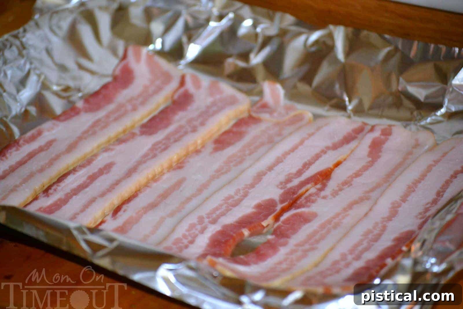 Raw bacon slices neatly arranged in a single layer on a foil-lined baking sheet, prior to cooking.