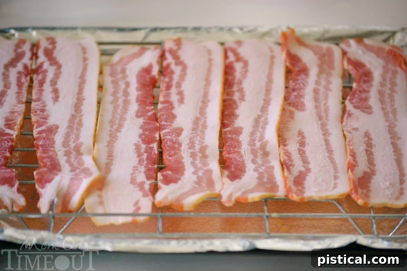 Bacon strips placed on a metal cooling rack over a baking sheet, illustrating the setup for elevated oven baking.