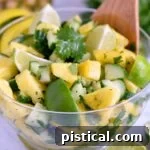 refreshing pineapple cucumber salad in clear plastic bowl with large wood serving spoon.