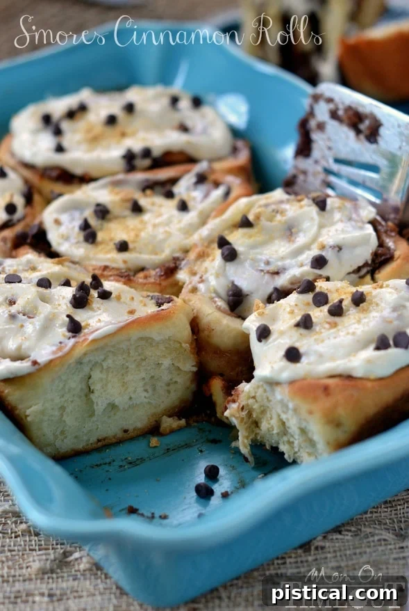 S'mores Cinnamon Rolls with Marshmallow Cream Cheese Frosting topped with graham cracker crumbs and mini chocolate chips, ready to be enjoyed