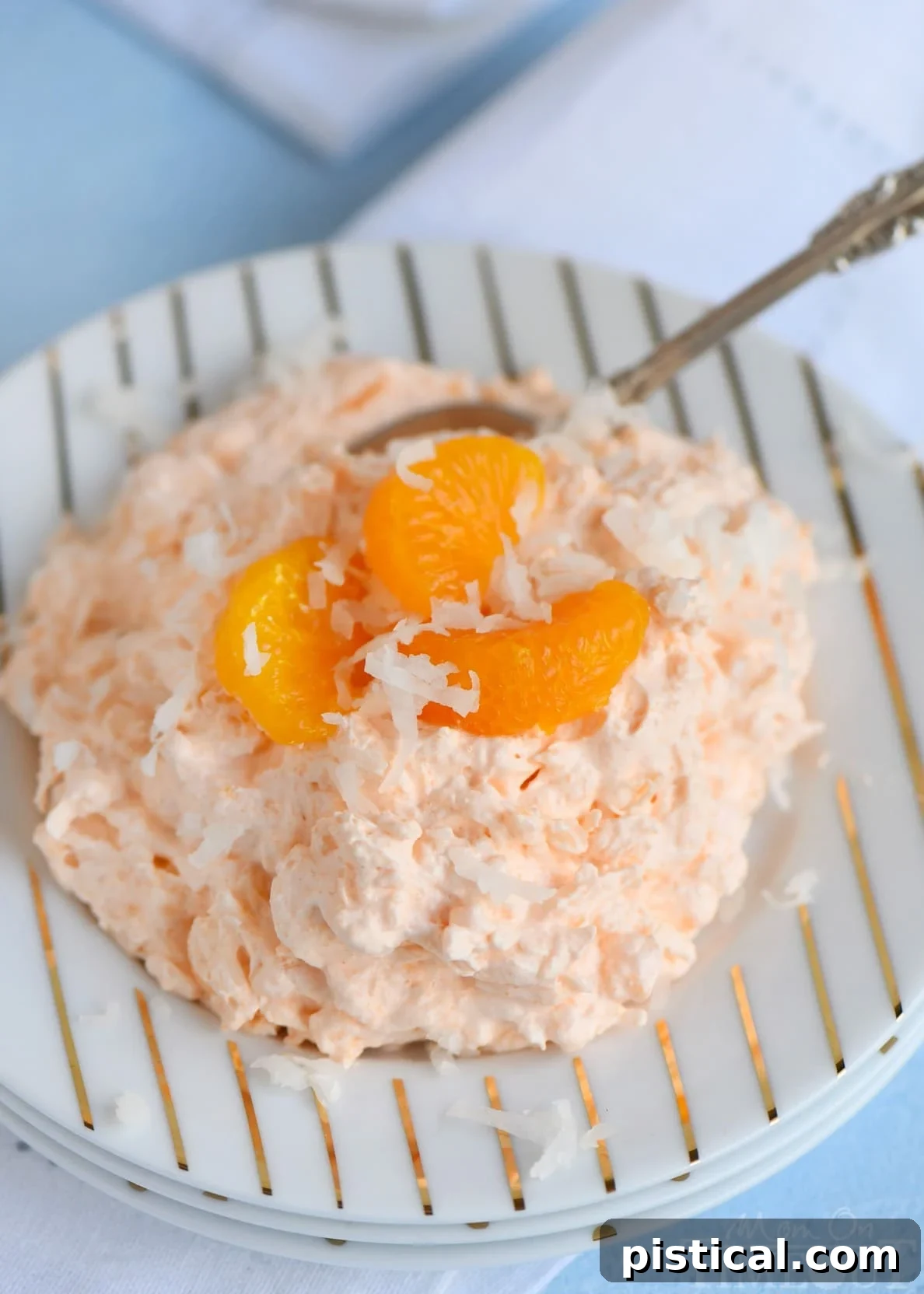 A close-up of the creamy, orange-hued Tropical Orange Jello Salad, showing bits of pineapple and coconut flakes, served in a decorative bowl.