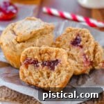 Two peanut butter and jelly muffins on a piece of parchment. One muffin has been split in half to reveal the jelly center.